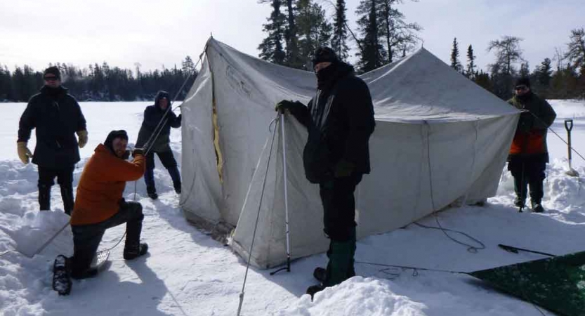 a group of gap year students work to set up a tent on a frozen, snowy lake
